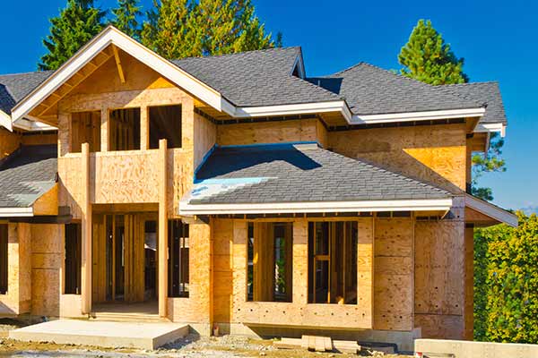Newly built home with gray shingles being installed on its roof